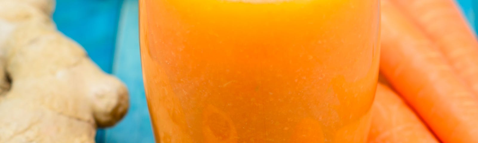 A glass of orange juice with some ginger, apricots, and carrots