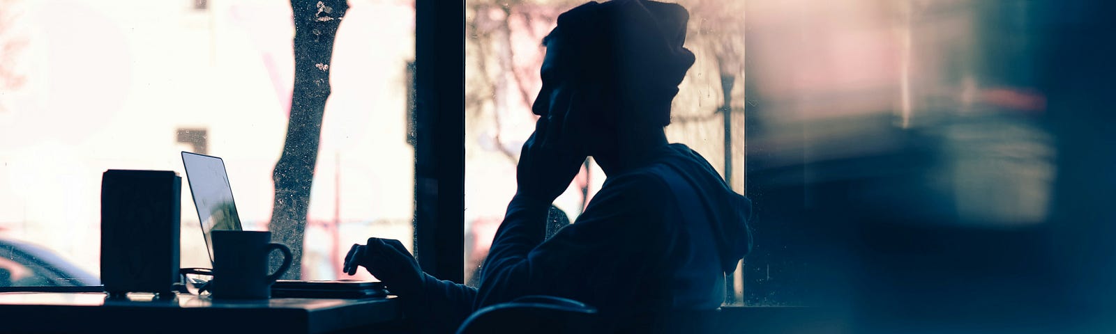 A person sitting in a cozy café, deep in thought while working on a laptop, capturing a moment of quiet reflection amidst a busy day.