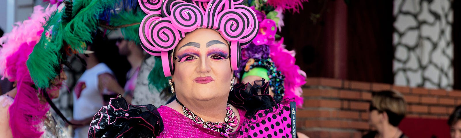 Drag Artist dressed in a flamboyant pink outfit with multi coloured feathers