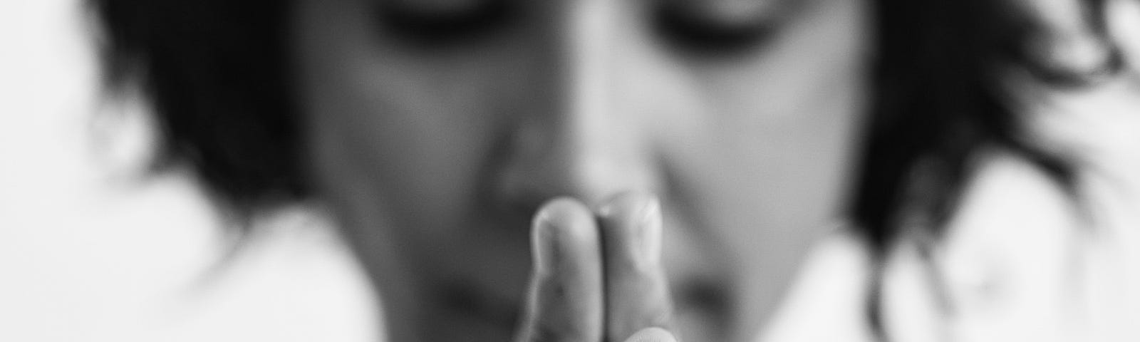 A woman with clasped hands saying grace before a meal.