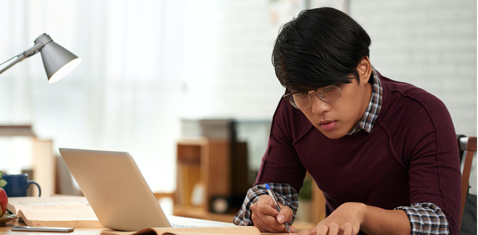 Young engineer wearing glasses and maroon sweater studying at computer