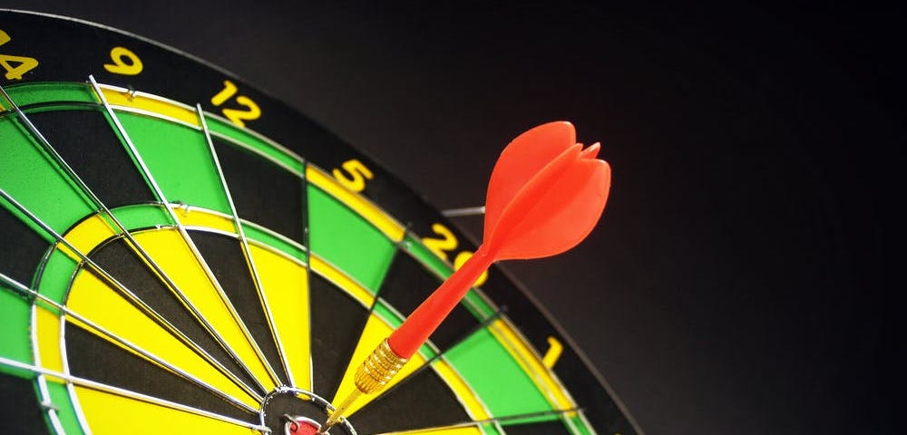 A green, yellow and black dartboard with a single red dart in the bullseye.