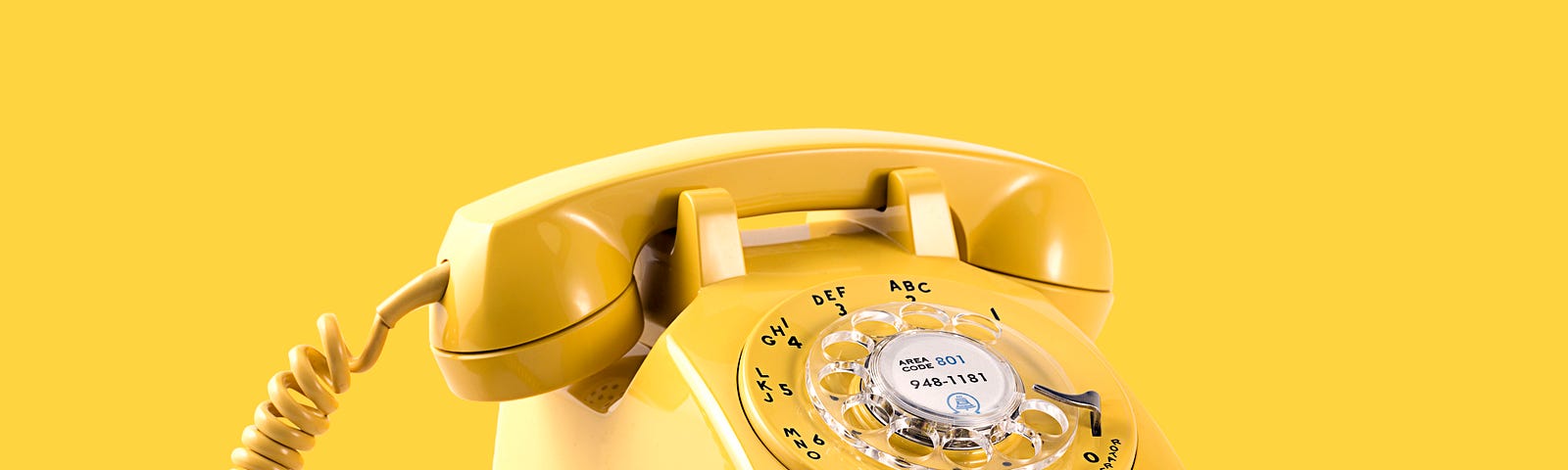 A bright yellow rotary phone on a flat yellow background.