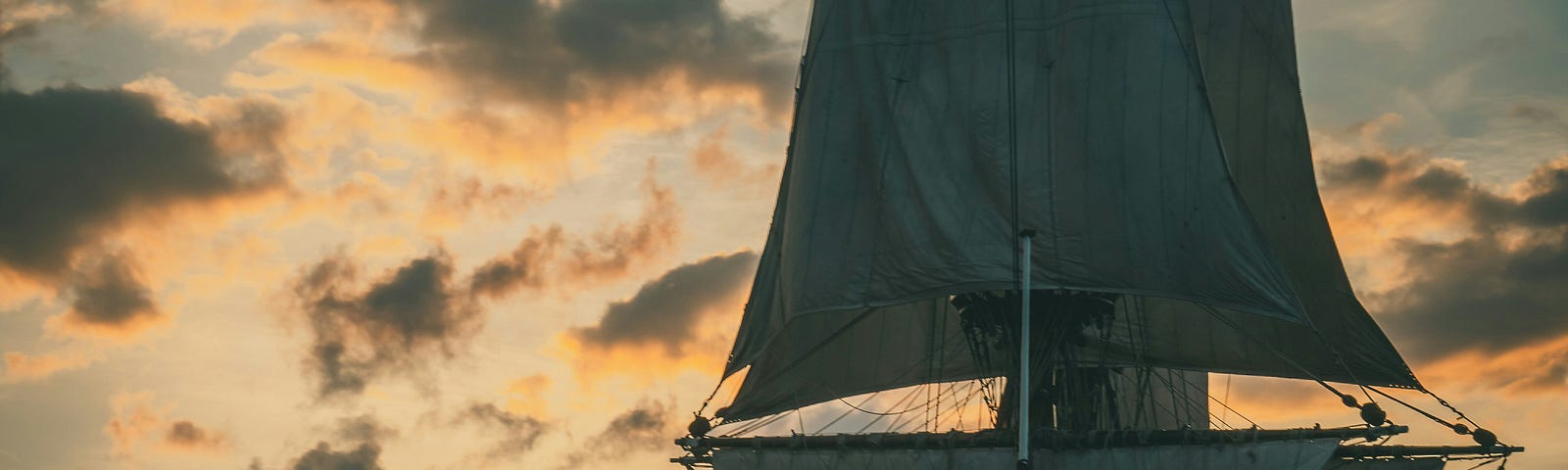 Photo: old-fashioned sailing ship on calm waters, before an orange sunset