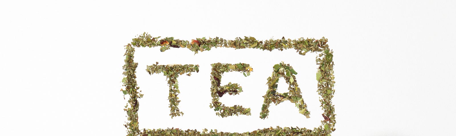 Tea leaves spell out the word “TEA” in capital letters, with more tea leaves framing the word in a rectangle. In the lower right of the image is a white cup half-filled with tea, seen from above. There is a white background.