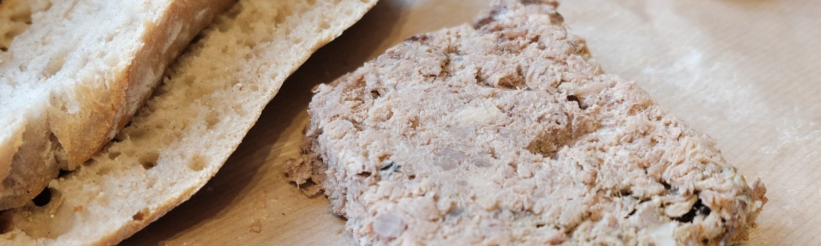 A block of pâté is seen beside a partly sliced loaf of rustic bread. There is also a knife, ready to spread the pâté on the bread— alt text to boost Medium stories