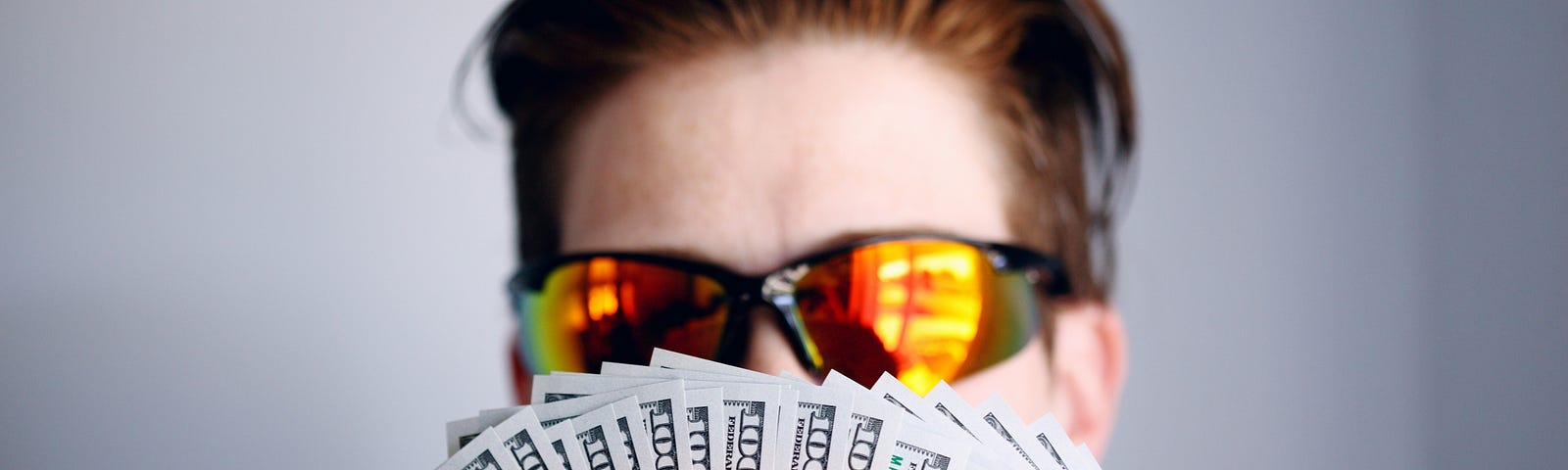A young man with glasses holding a lot of money in his hands