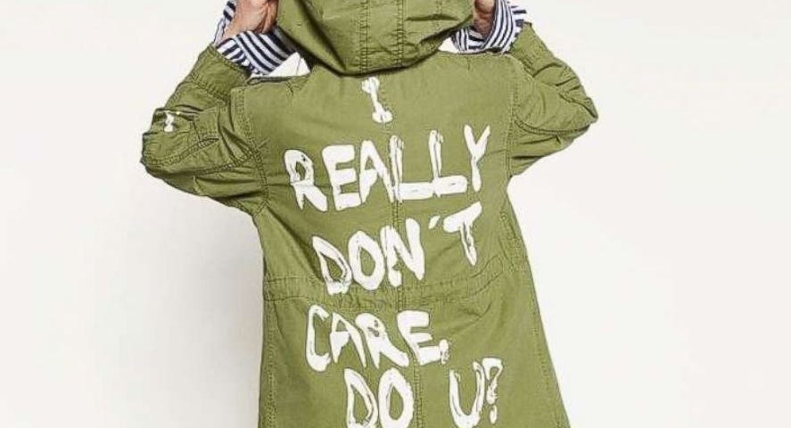 Zara model wearing green jacket famously worn by Melania Trump. White block graffiti says “I really don’t care do u?”