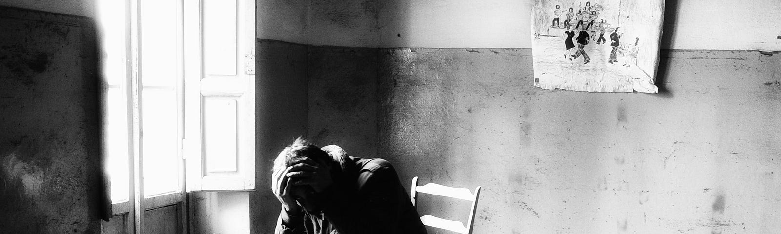 A man holds his head in his hands in a shabby room, black and white photo