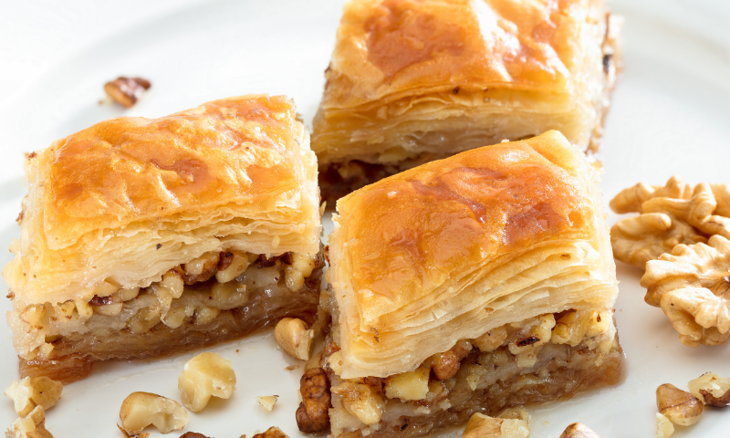 Three portions of Albanian Baklava surrounded by walnut pieces on a white plate.