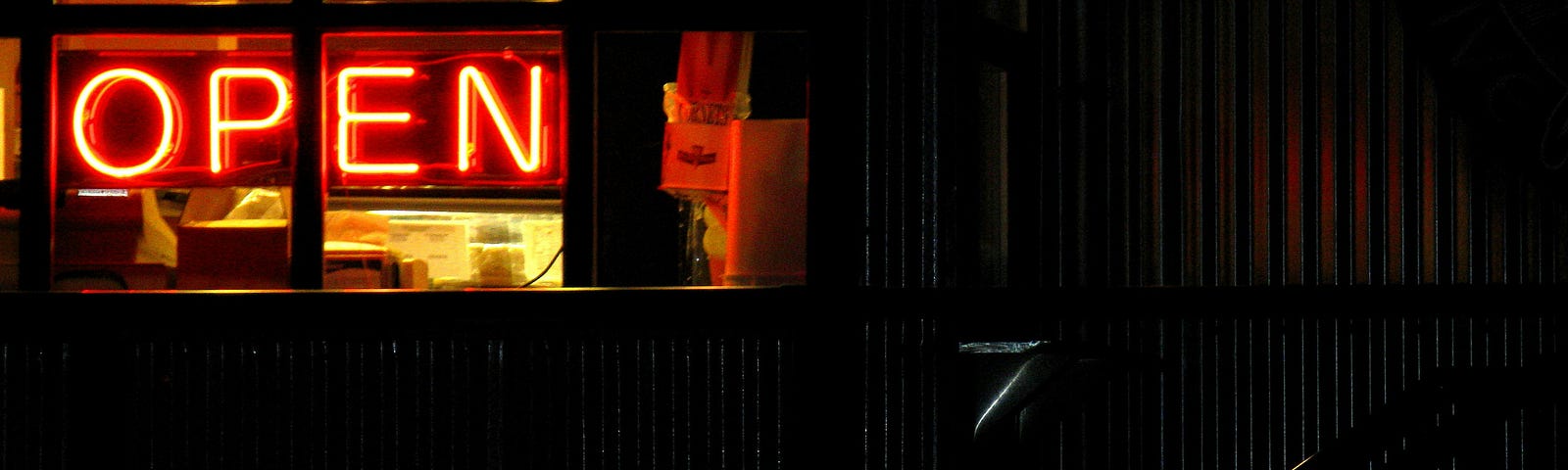 a red neon open sign in the window, its nighttime