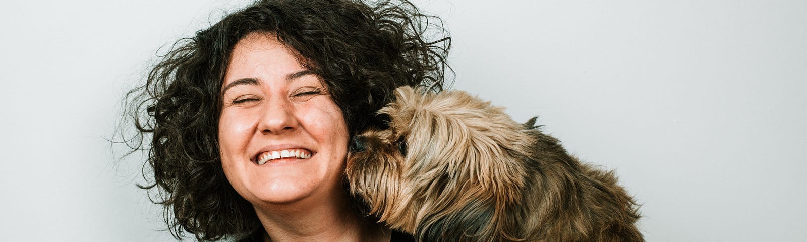 A woman smiling as she holds a dog close, the dog licking at her face.