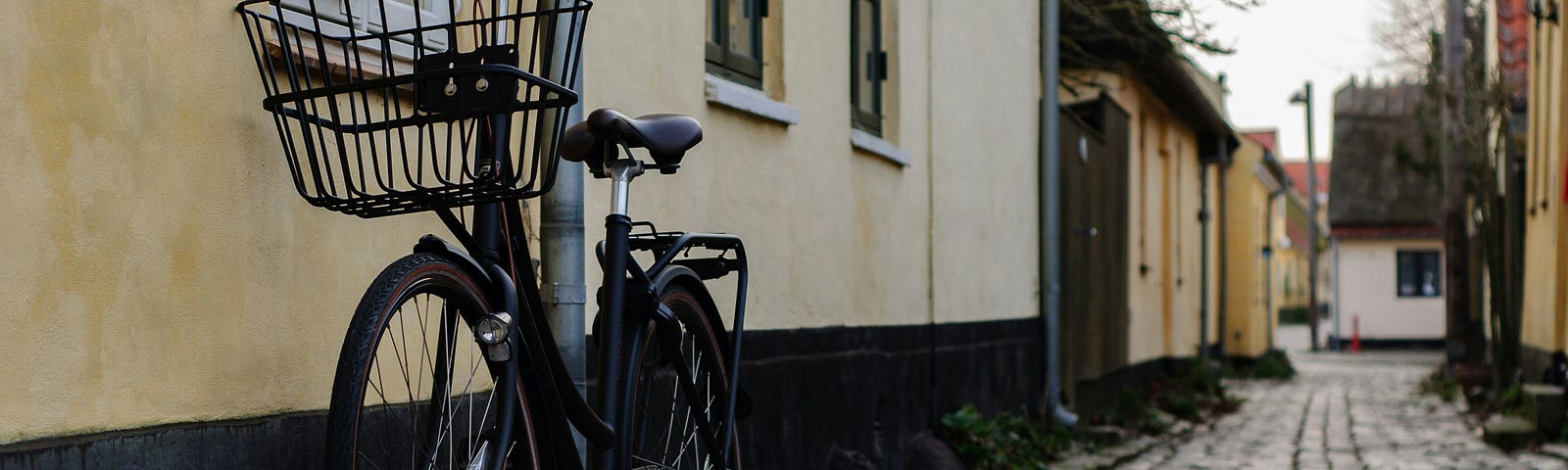 A vintage bycicle painted in black parked next to a yellow house.