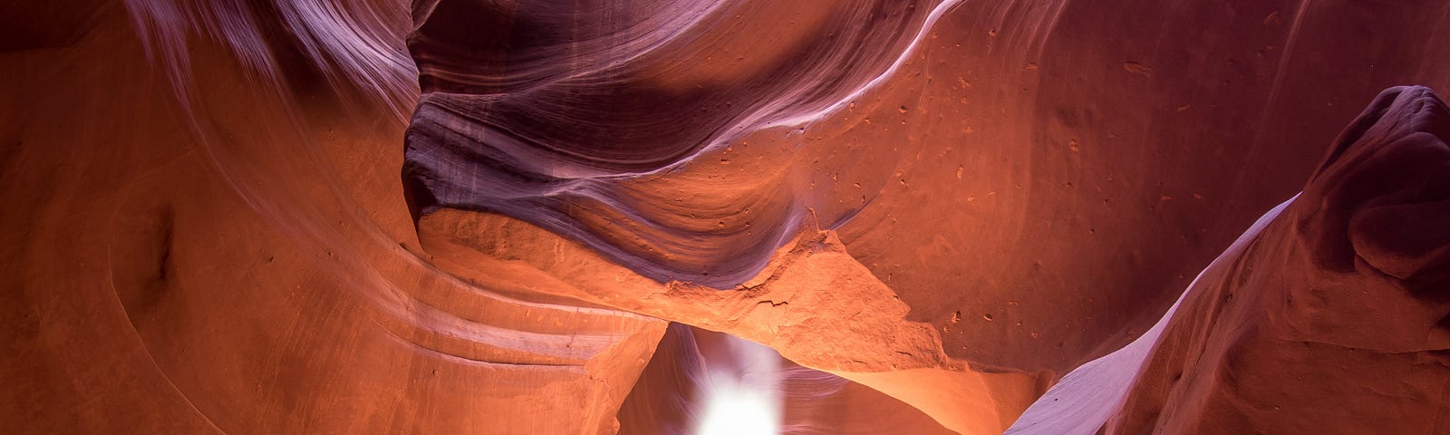 Through a hole in the cavrern, a shaft of light illumines swirling configurations in the red rock.