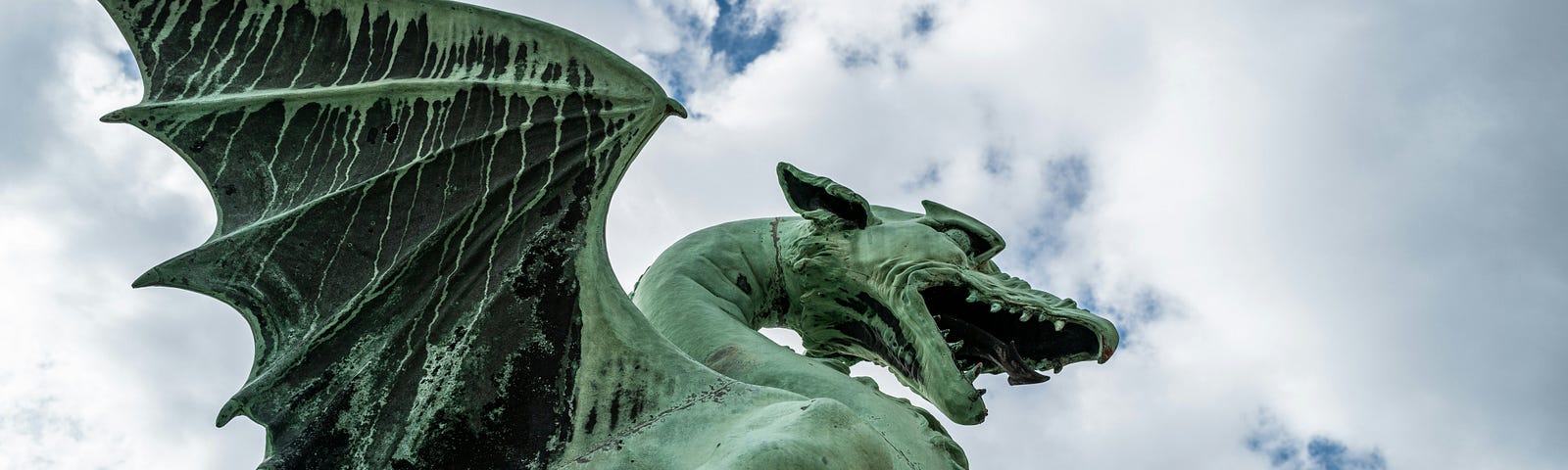 A green statue of a dragon seen from a low angle against a cloudy sky