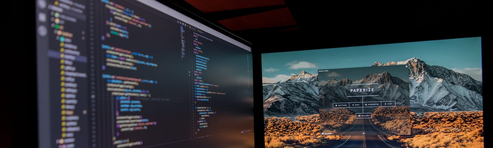 Two monitors with an open Visual Studio Code editor and a mountain wallpaper