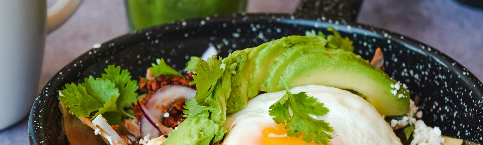 A bowl of tempting avocado slices, cotija cheese, and cilantro topped with a soft-poached egg.