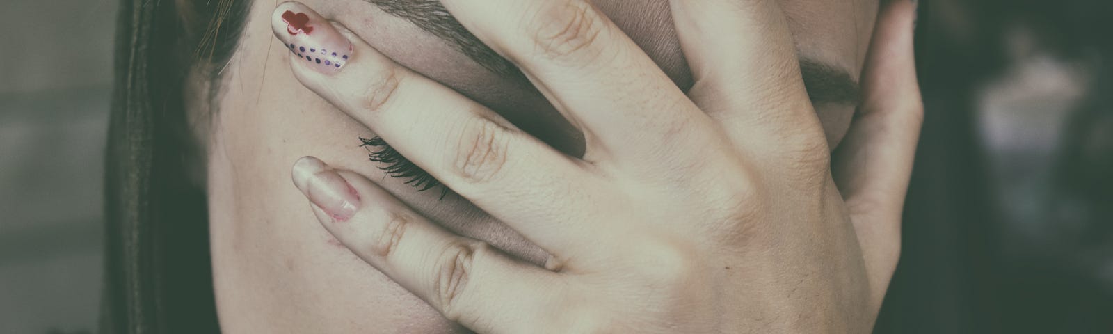 Image of a woman holding a hand in front of her face, as if in pain.