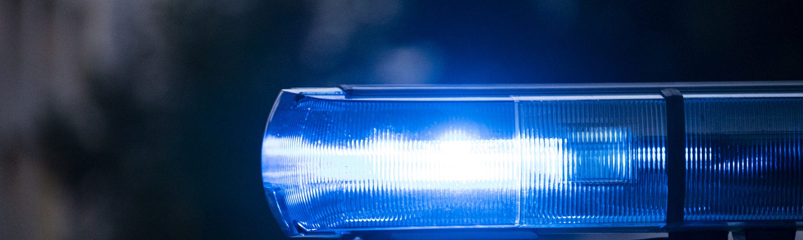 Blue light on a police car shining into the darkness.