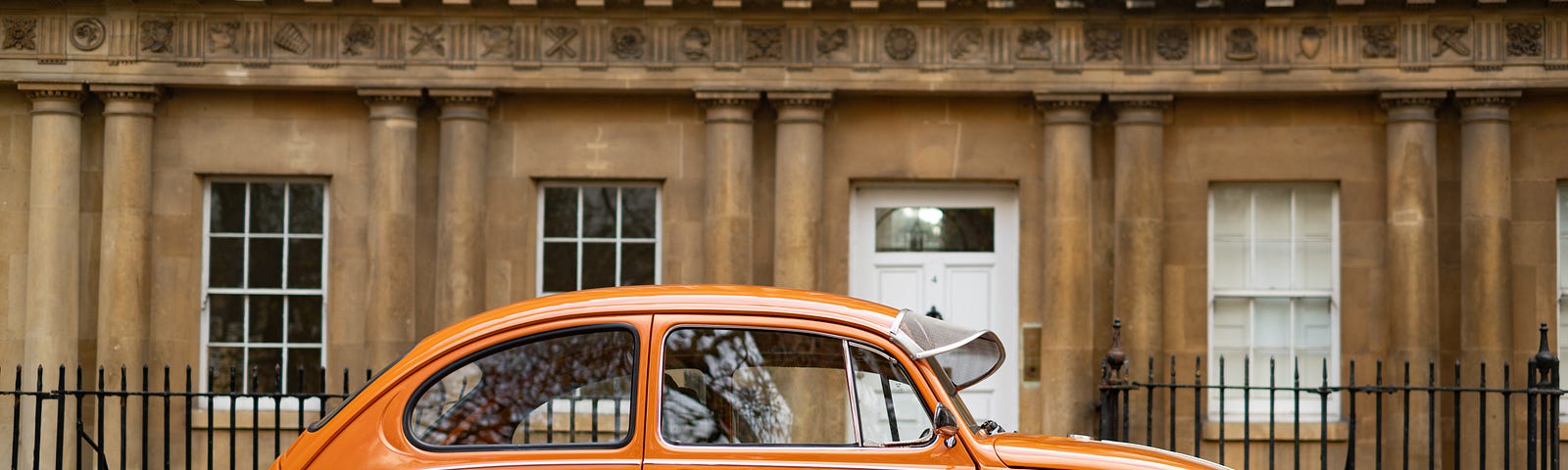 An orange Beatle car parks in from of a building.