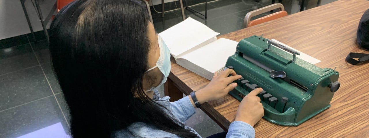 Roxana Alemán sentada escribiendo en Braille ante una máquina Perkins.