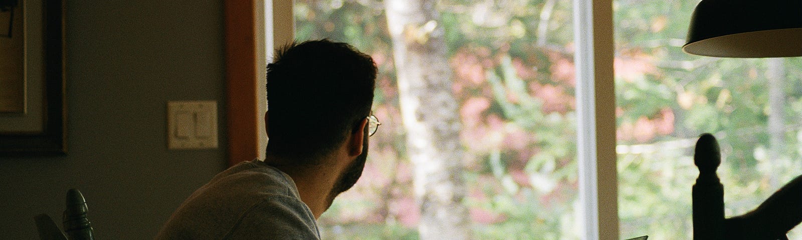 A guy working from home. Looking out of the window, involved in deep thought.