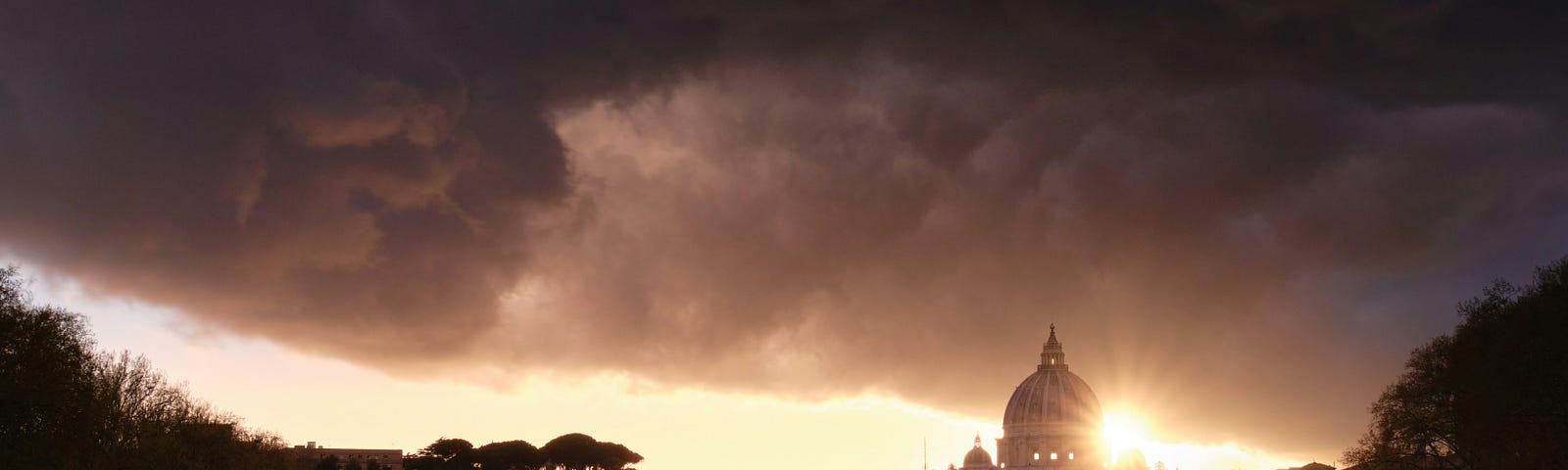 A photo by Joshua Kettle on Unsplash of the Tiber river in Rome with a low sun and dark clouds behind St. Peter’s Basilica.