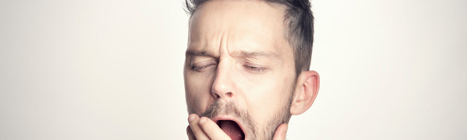 A man in a white background yawning because he has to work.