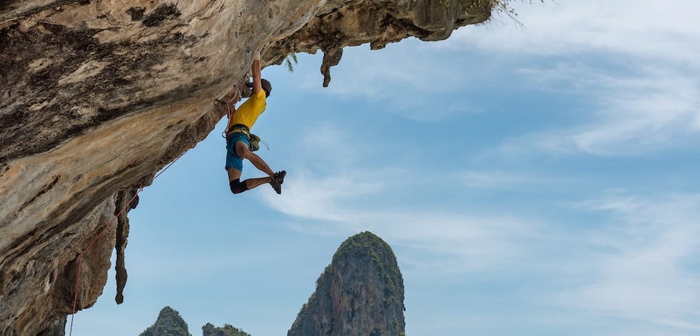 Man climbing cliff above water in Thailand