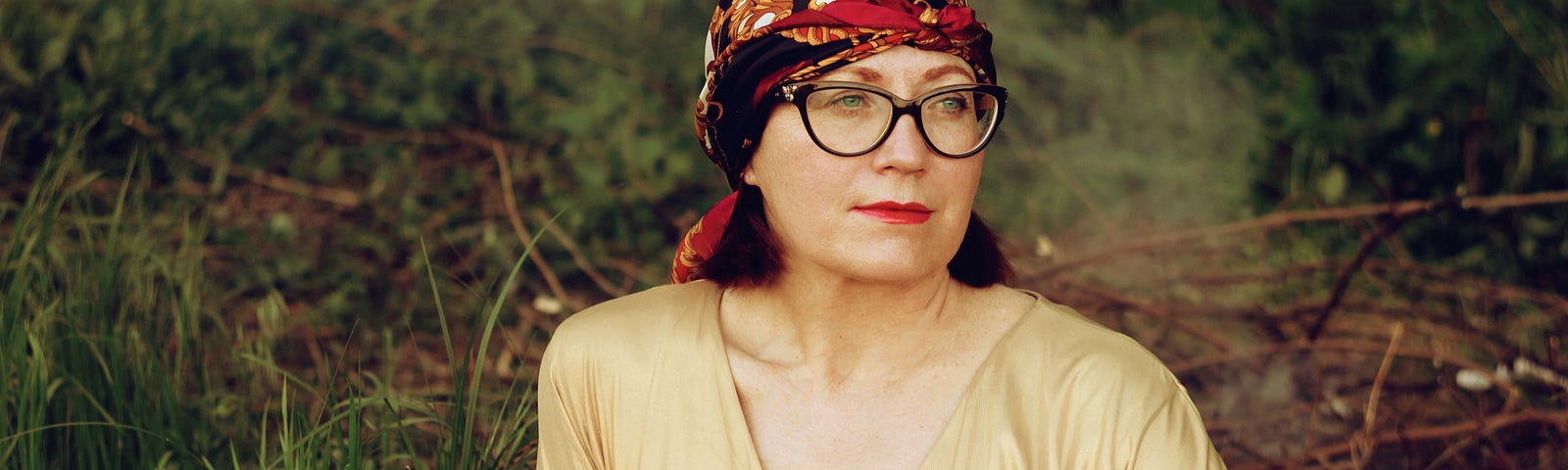 A woman in a bright yellow shirt, glasses and a red head scarf looks off to the side