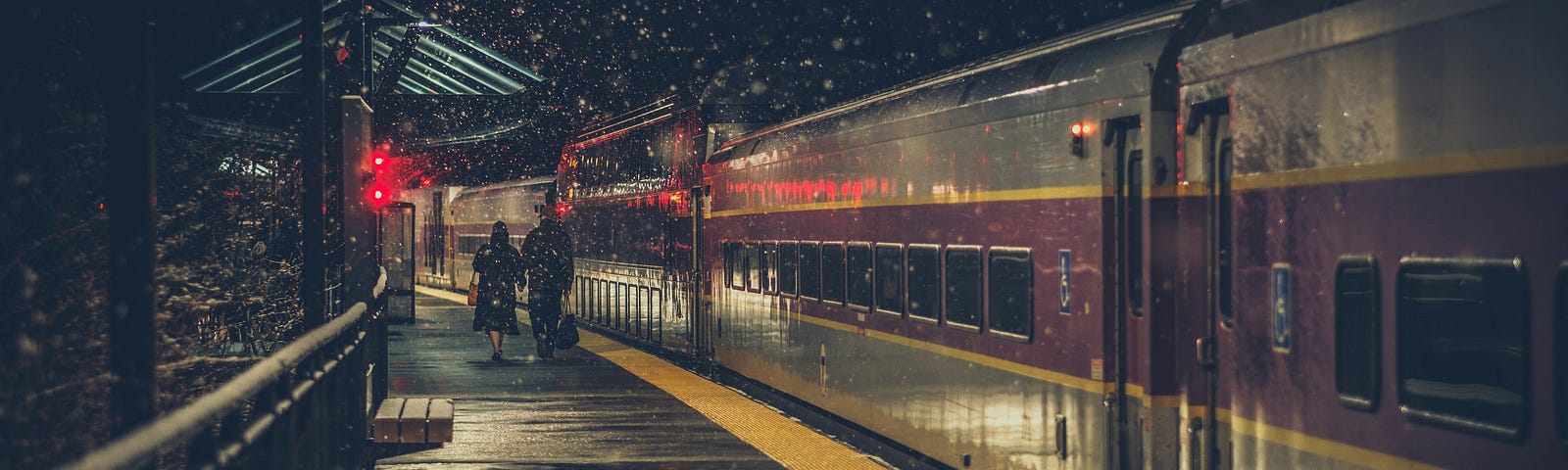 Train sitting at the station on a dark, rainy night, with two people walking away in the distance.