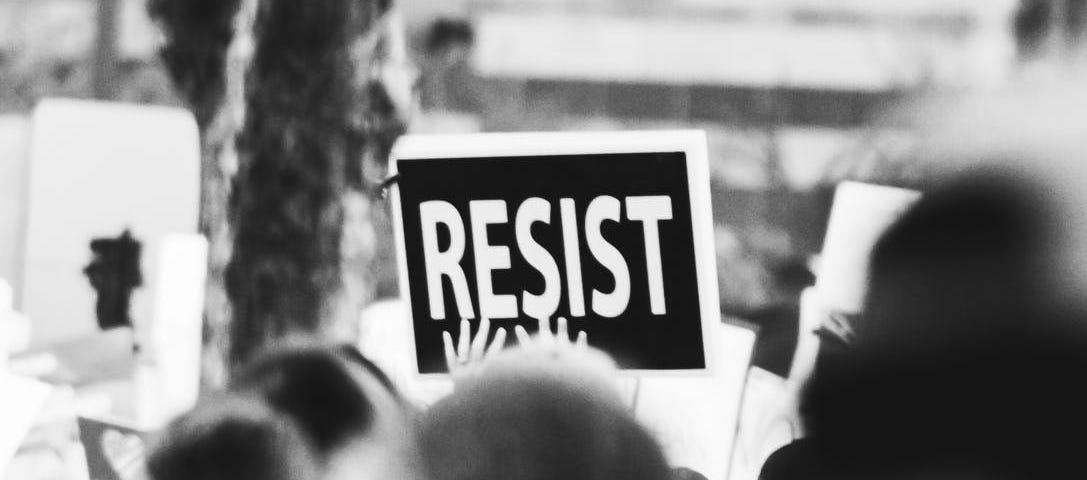 A protest sign saying “Resist” raised above people in the foreground.