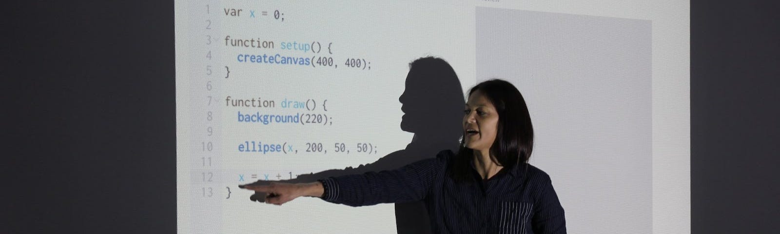 Asian-American woman with long dark hair stands in front of a projection of p5.js editor.