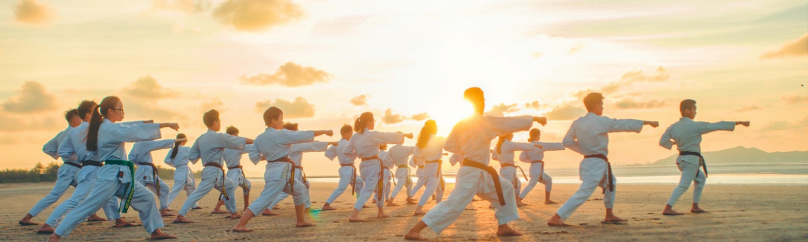 Group of students in white doing taekwondo on the beach