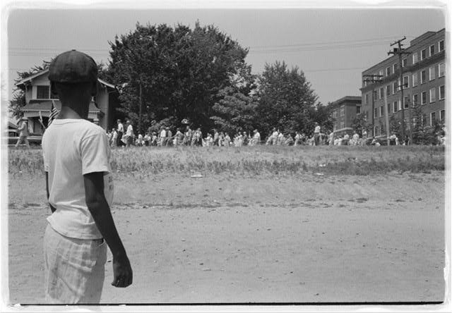 “Little Rock, 1959. Mob marching from capitol to Central High,” 1959. Photograph shows a young African American boy watching a group of people, some carrying American flags, march past to protest the admission of the “Little Rock Nine” to Central High School. Courtesy Library of Congress, Prints and Photographs Division. Photo: John T. Bledsoe