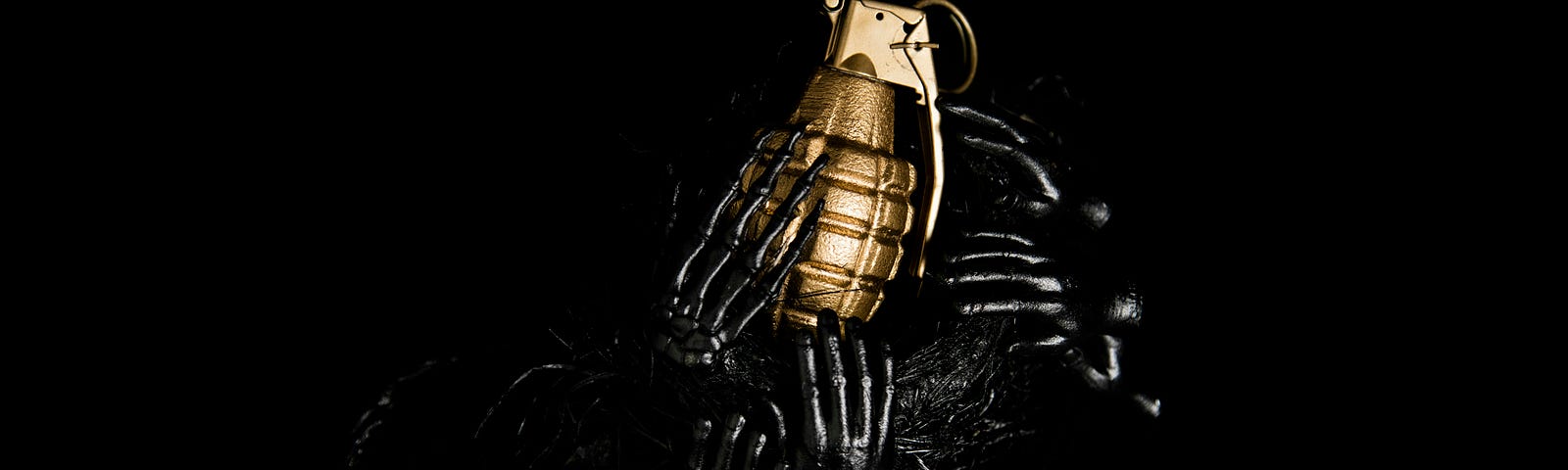 A golden hand grenade held by tiny hands of blackened metal