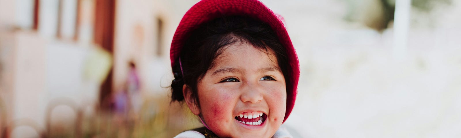 A happy child wearing a red bonnet, a checkered red and white coat, and a joyous smile.