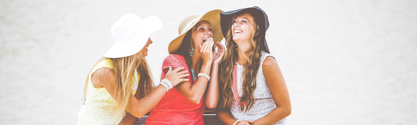 Three woman in sunhats leaning in and appearing to be gossiping about something