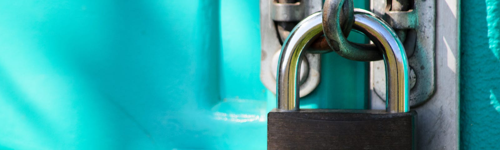 A rusted silver padlock holds together two bright teal doors.