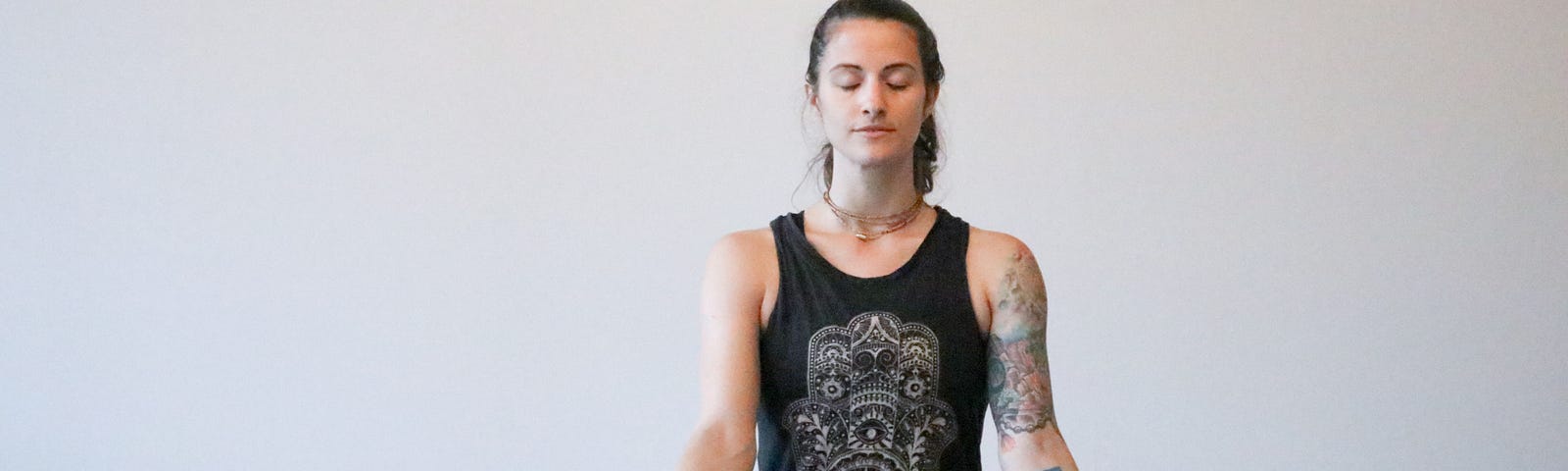 A woman, seated, in a yoga pose, breathing with her eyes closed.