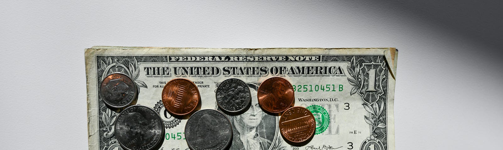 A dollar bill with several coins on top of it.