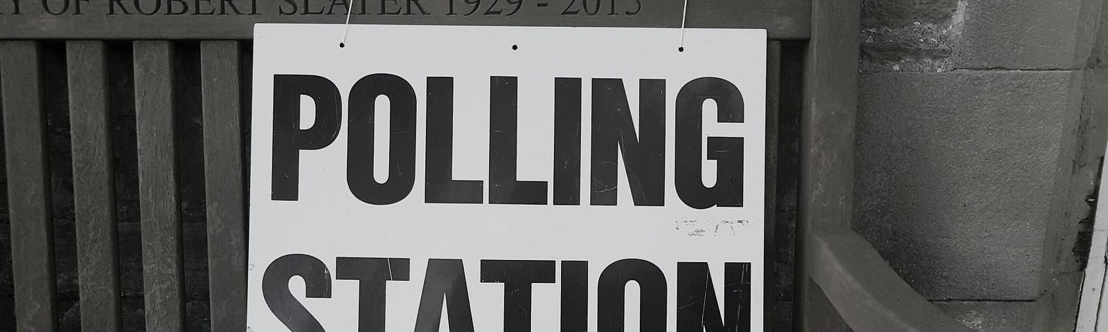 Black and white sign with “Polling Station” in black bold letters on a white background hung on a bench.