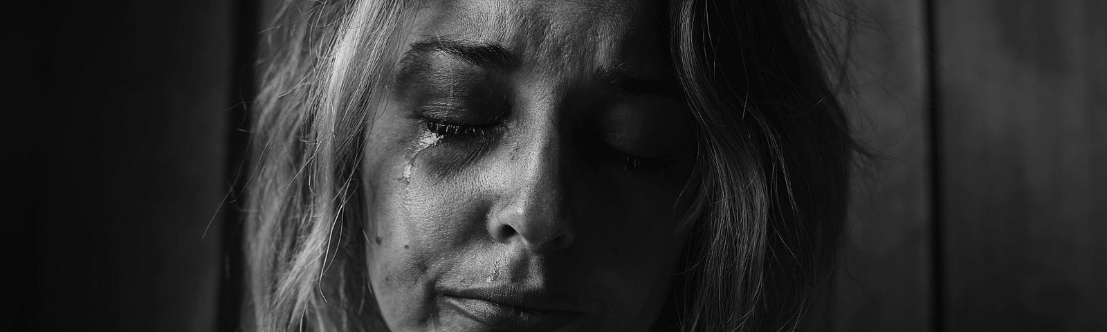 It’s a black and white picture of a woman crying. She has her right hand on her left shoulder.