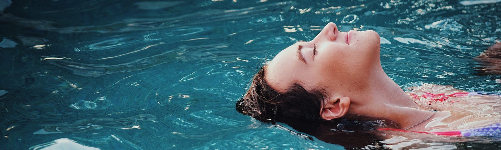 Here is a photo of a young woman floating in a peaceful pool of water, experiencing deep tranquility and rest.