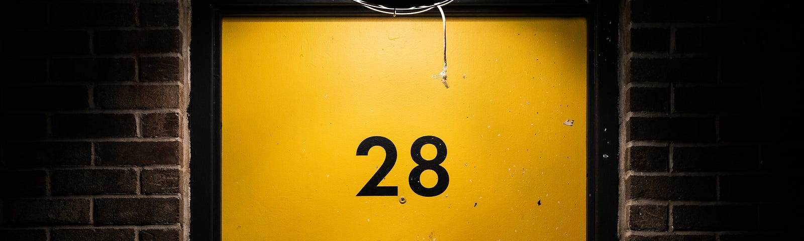 A harshely lit yellow door, with the number 28 on it.