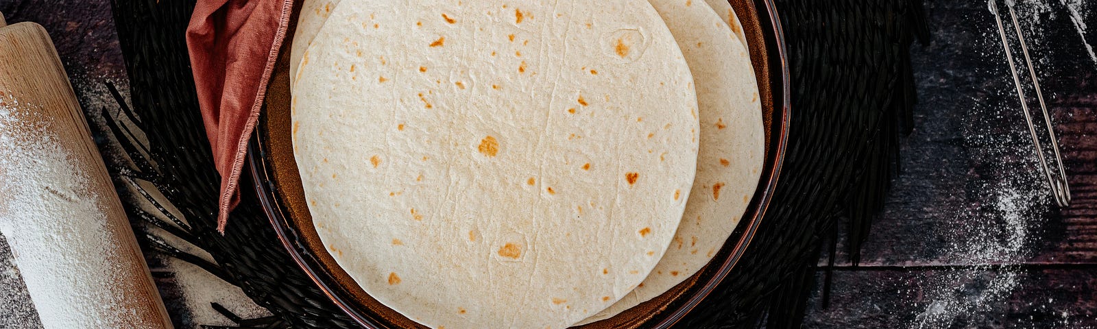 a bowl of fresh flour tortillas, with a rolling pin at the left.