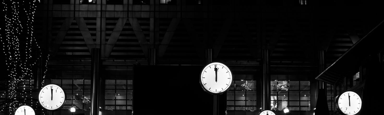 A black and white background of either buildings or stairs with several clocks indicating midnight.