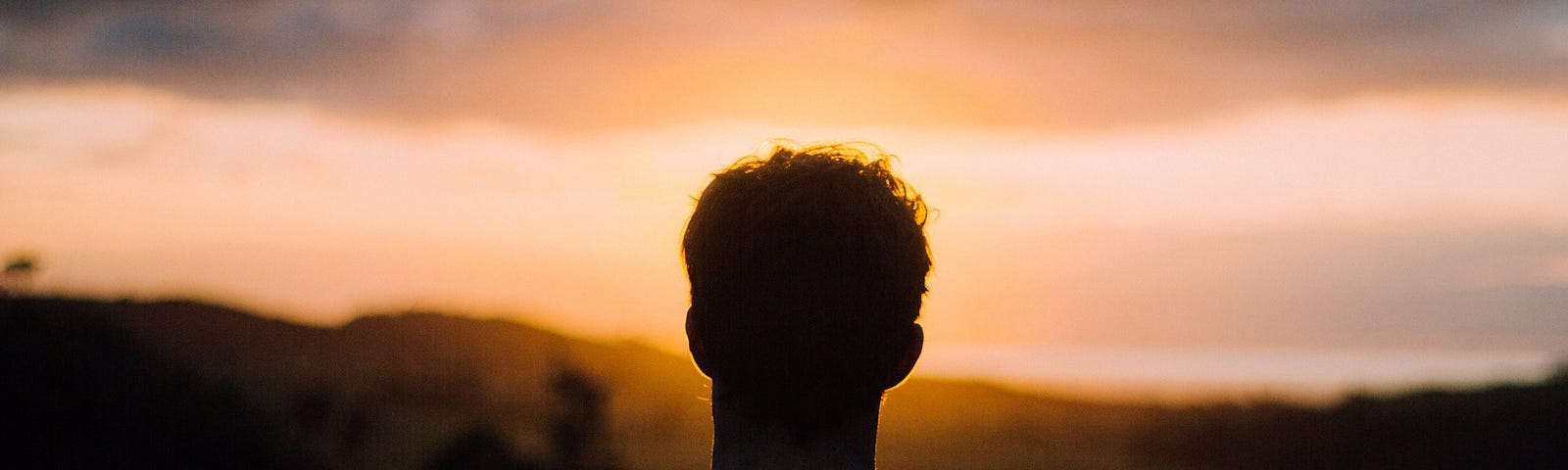 Photo of a young man in shadow watching the sunrise.