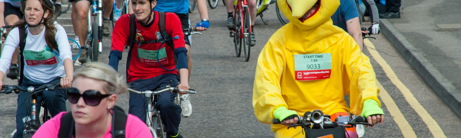 Person riding a pushbike in a crowd dressed in a chicken suit.