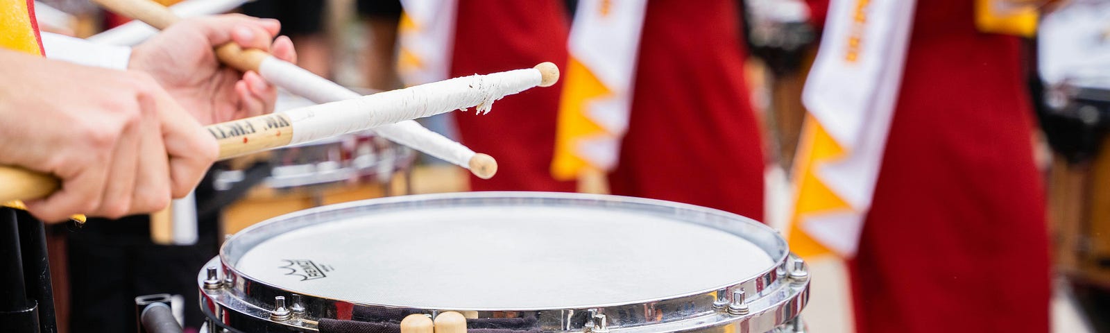 A close-up shot of a drummer in a college band with just his hands and drumsticks getting ready to play the drum before marching onto the field to perform.